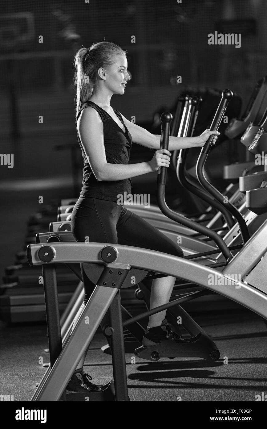 Junge Frau im Fitness-Studio trainieren. Auf auf einem Computer ausführen. Joggen im dunklen Fitnessclub trainieren. Cardio. Schwarz und weiß. Stockfoto