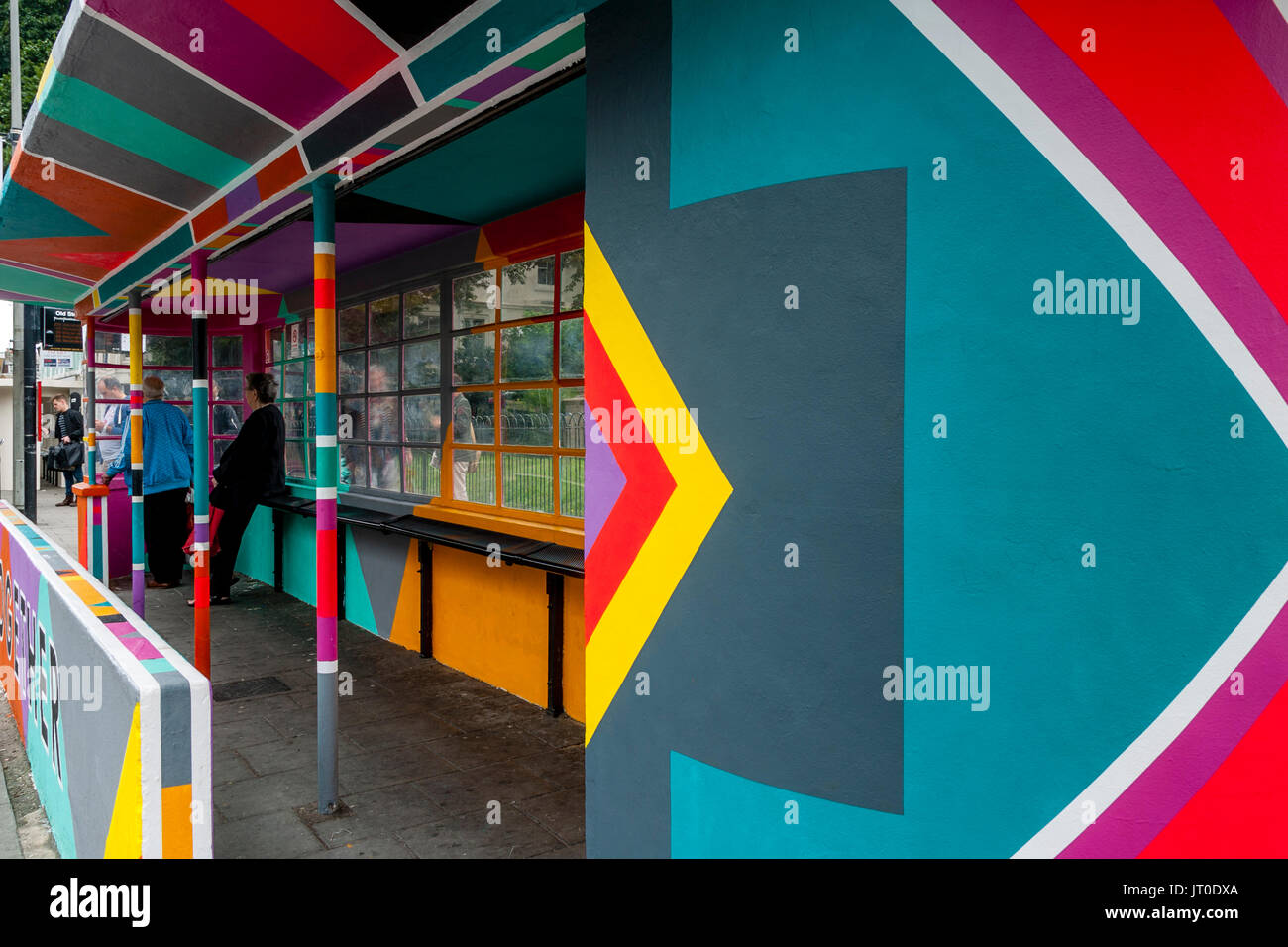 Die Menschen warten auf einen Bus in einem bunt bemalten Bus Shelter, Brighton, Sussex, UK Stockfoto
