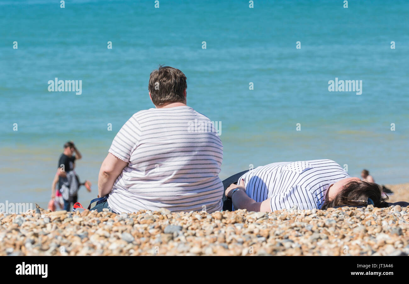 Übergewichtige Frau sitzt auf einem Strand. Große Dame saß in der Sonne am Strand in Großbritannien. Übergewichtige Person an einem Strand. Stockfoto