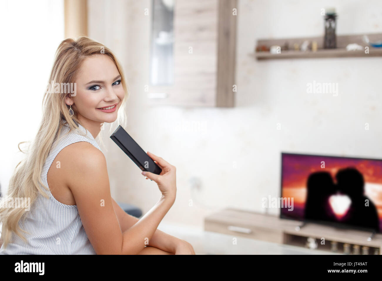 Glückliche junge Frau beobachten romantischen Film im Wohnzimmer Stockfoto