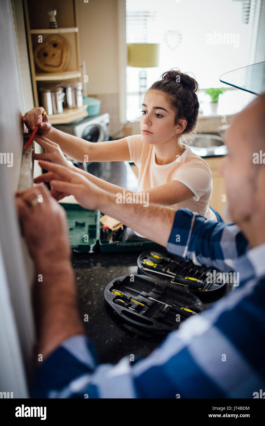Teenage Mädchen ihren Vater mit DIy zu helfen in Ihrer Küche. Das Mädchen ist die Kennzeichnung der Wand mit einem Bleistift. Stockfoto