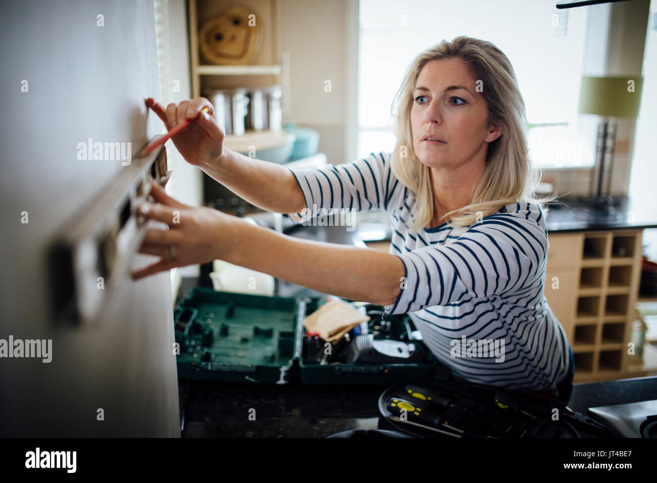 Reife Frau mit Hilfe einer Wasserwaage und Markierung der Wand mit einem Bleistift in Ihrer Küche. Stockfoto