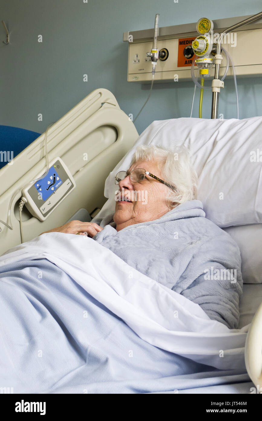 Eine ältere Dame in einem Krankenhausbett warten auf ein Care Paket zu ermöglichen ihre Entlastung. Stockfoto