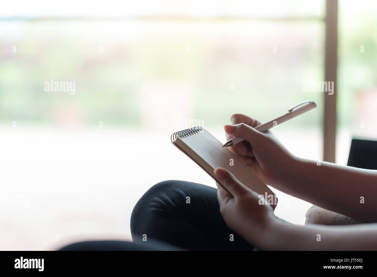 Frau Hand schreiben einige Idee, auf kleinen Notizblock beim Sitzen auf Stuhl im Haus. Freie Arbeiten von überall Konzept Stockfoto