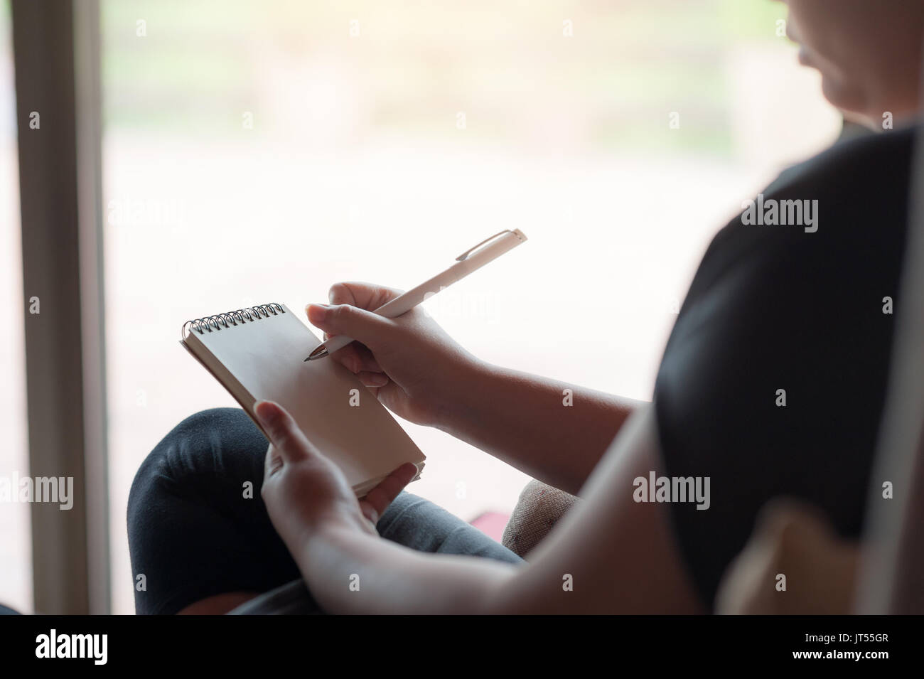 Frau Hand schreiben einige Idee, auf kleinen Notizblock beim Sitzen auf Stuhl im Haus. Freie Arbeiten von überall Konzept Stockfoto