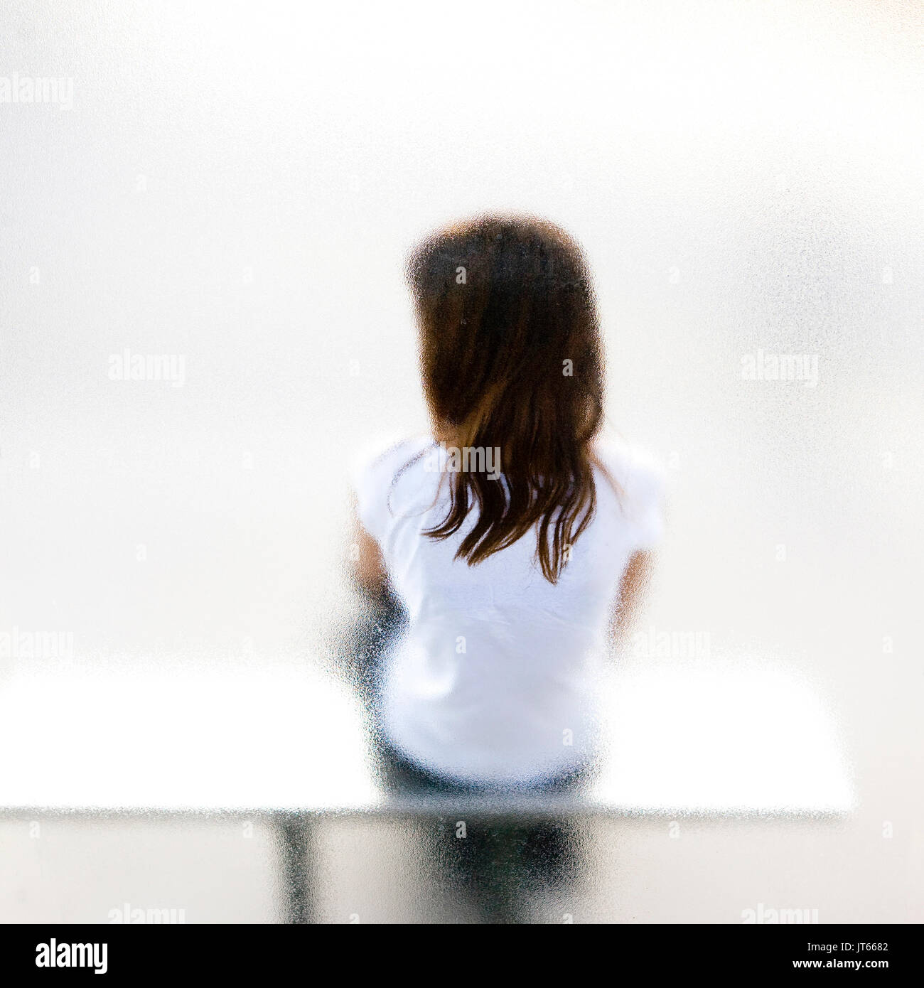 Junge Mädchen, die auf einer Bank sitzen, allein, gesehen aus einem Fenster Stockfoto