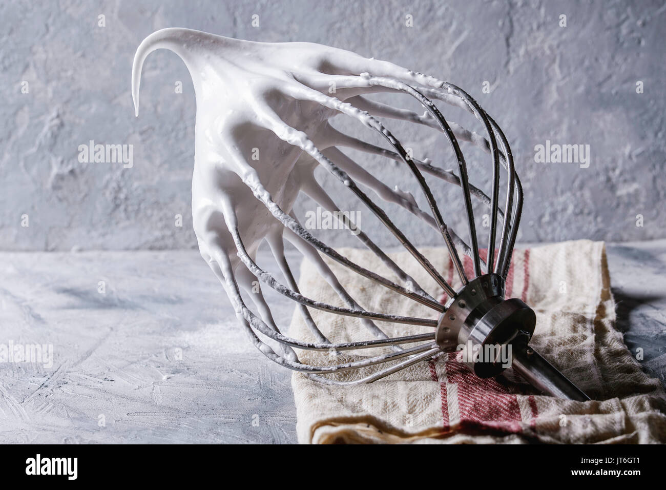 Prozess des Kochens Meringue. Geschlagener Eischnee auf mixer Quirl auf leinen tuch über grau Textur Hintergrund. Backen dessert Konzept. Nahaufnahme Stockfoto