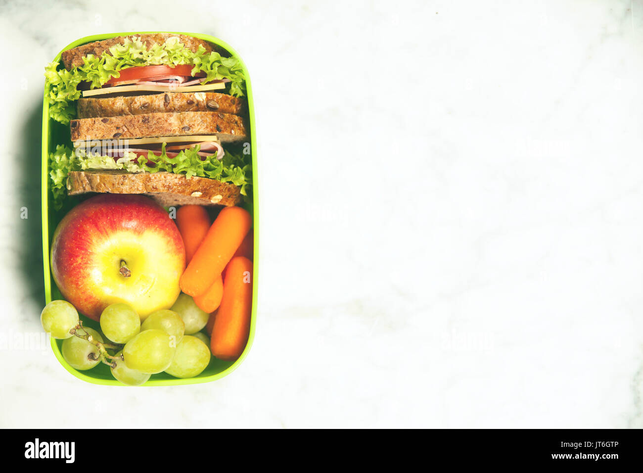 Grüne Schule Lunch Box mit Sandwich, Apfel, Traube und Karotte schließen bis auf weißem Hintergrund. Gesunde Essgewohnheiten Konzept. Stockfoto