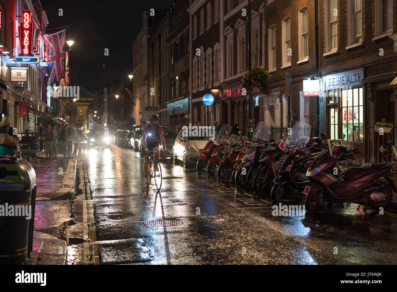 Ein Blick auf eine Reihe von Mopeds und ein Radfahrer auf der Dean Street in Soho in London in einer regnerischen Nacht. Aus einer Reihe von Fotos in einer regnerischen Nacht in Soho, Lon Stockfoto