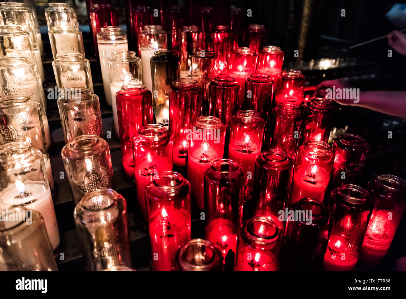 Rote und weiße Votivkerzen mit gelber Flamme in der Kirche mit Hand ihnen Beleuchtung Stockfoto