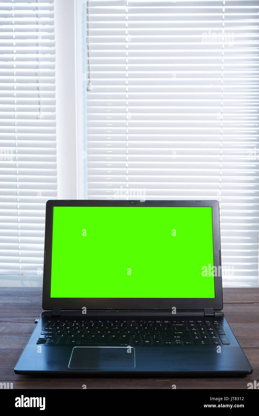 Laptop in kleinen Büros zu Hause am Schreibtisch aus Holz mit Green Screen auf dem Display und viel Platz kopieren. Vertikaler Stockfoto