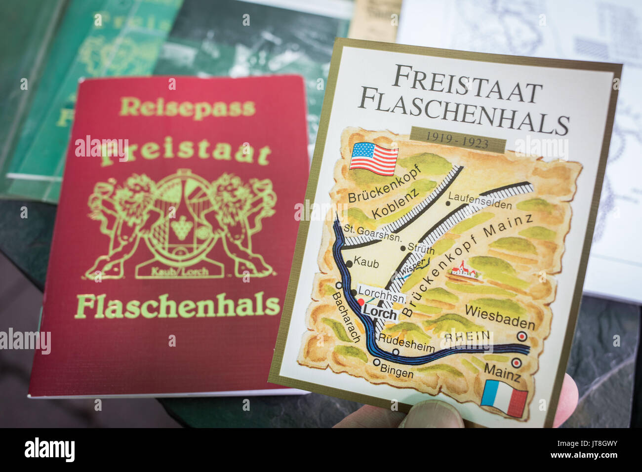 Kaub, Deutschland. 27. Juli, 2017. Peter Josef Bahles, der Präsident und Gründer der Freistaat Flaschenhals Initiative, hält einen Reisepass (L) und einen Wein Etikett eingeführt, nach dem Ersten Weltkrieg im Freistaat Flaschenhals, einem Landstrich aus dem Rest von Deutschland, kurz ein Staat in seiner eigenen wurde direkt danach wurde durch den Entente-mächten zwischen 1919 und 1923, in Kaub, Deutschland, vom 27. Juli 2017 Links extern scharf getrennt. Die Geschichte der Freistaat hat eine touristische Attraktion in der Gegend geworden. Foto: Frank Rumpenhorst/dpa/Alamy leben Nachrichten Stockfoto