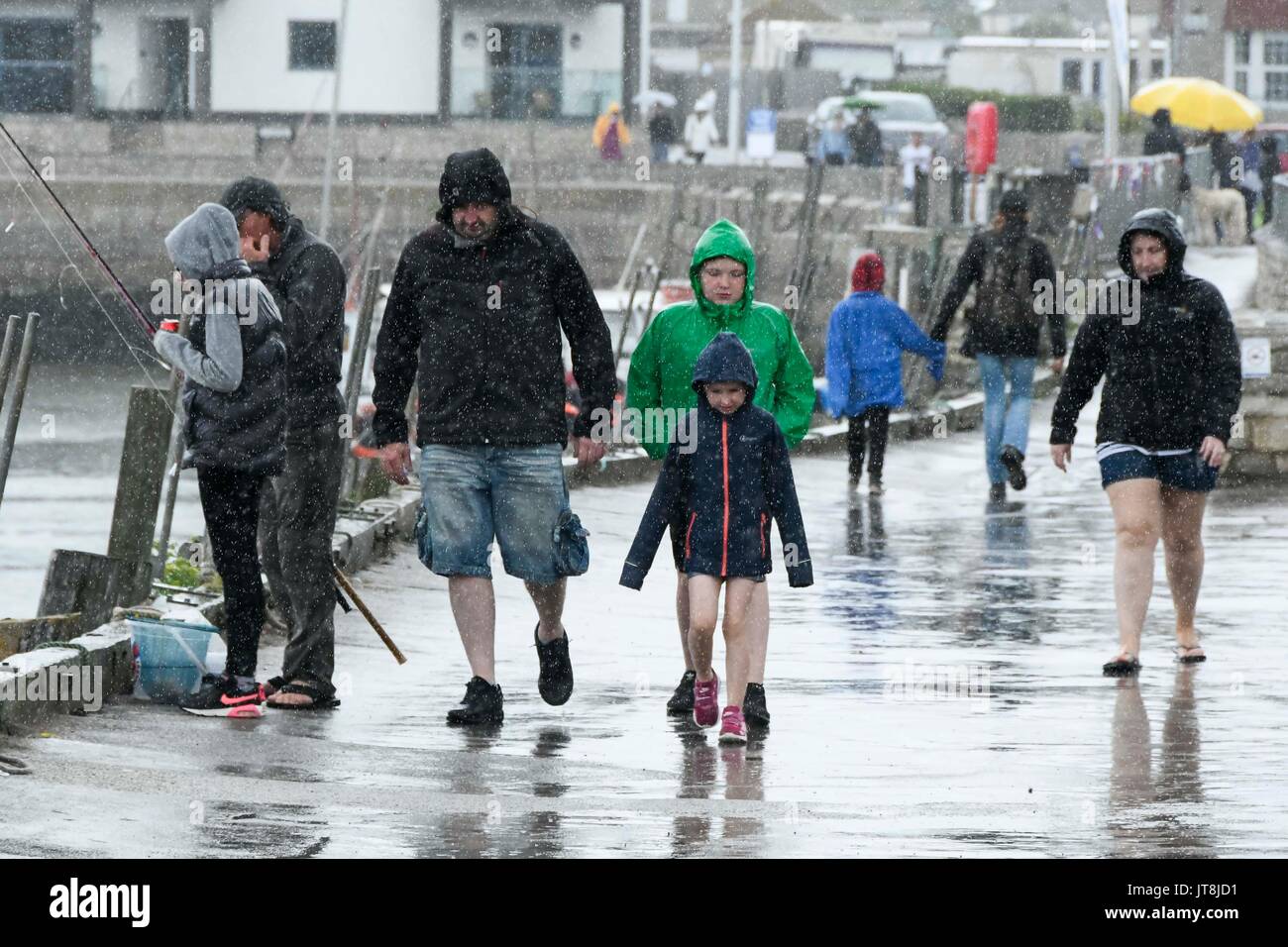 West Bay, Dorset, Großbritannien. 8 Aug, 2017. UK Wetter. Eine Familie einen Spaziergang entlang der Hafenpromenade in den Badeort West Bay in Dorset mit regen Mäntel auf wie ein schwerer Regen fällt. Photo Credit: Graham Jagd-/Alamy leben Nachrichten Stockfoto