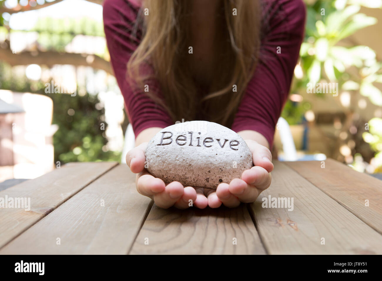 Junge Frau an einem Holztisch im Hintergrund sitzen mit einem Felsen vor ihr, mit dem Wort bezeichnet Glauben. Model Release Stockfoto