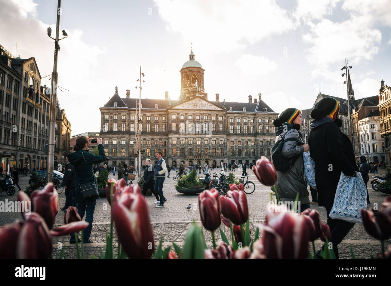 Amsterdam, Niederlande - 25 April 2017: Royal Palace auf dem Dam Platz auf dem Hintergrund der Paar Tourist in rastaman Hüte und Tulpen in den Abend. Stockfoto