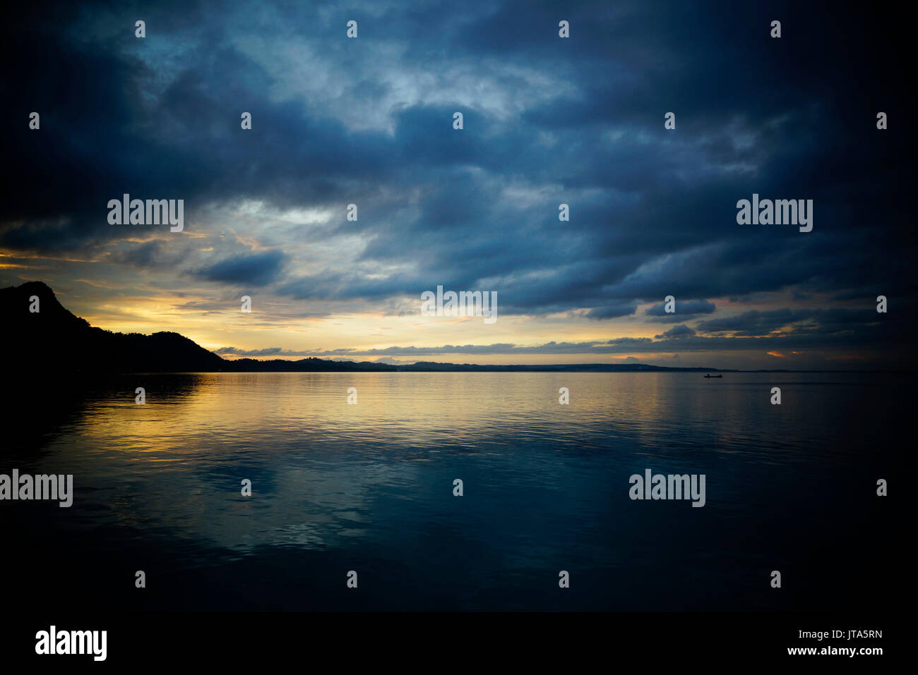 Silhouette der kleinen Boot mit einer Person unter Dunkelblau stürmischen Himmel von Wolken in Richtung Insel im asiatischen Ozean bei Einbruch der Dunkelheit, während Gelb sunse Stockfoto