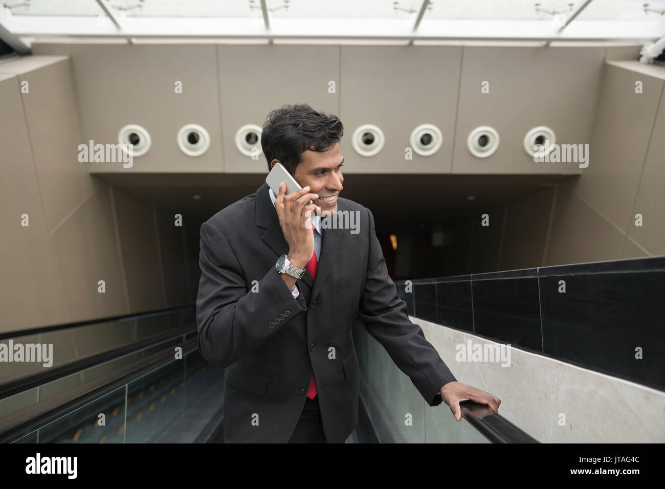 Indische Geschäftsmann mit seinem Smart Phone beim Stehen auf einer Rolltreppe in der Stadt. Stockfoto