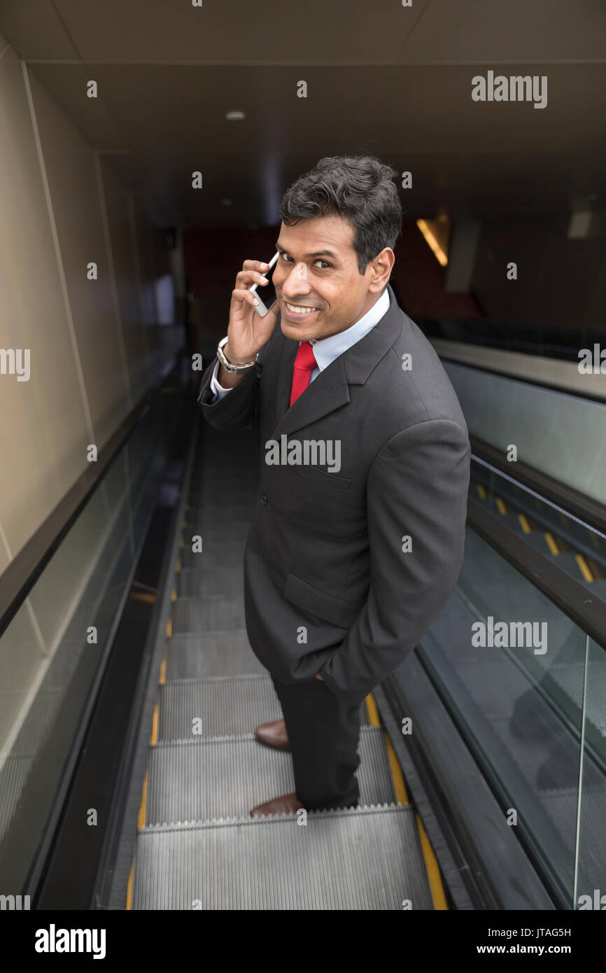 Indische Geschäftsmann mit seinem Smart Phone beim Stehen auf einer Rolltreppe in der Stadt. Stockfoto