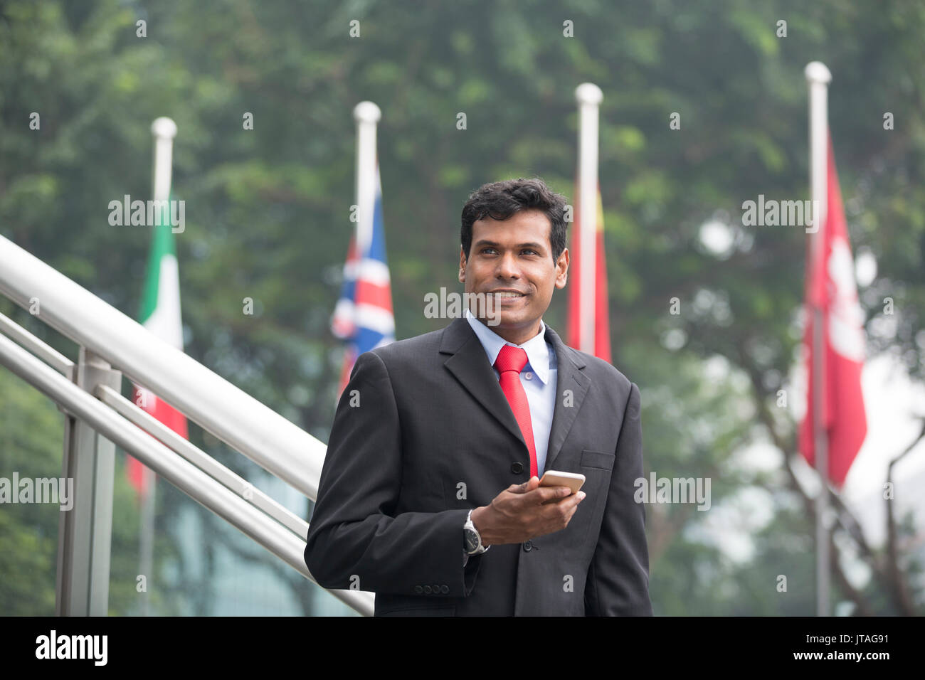 Indische Geschäftsmann mit einem Smart Phone, vor Flaggen. Porträt eines asiatischen Geschäftsmann lächelnd, ein Smart Phone, vor Flaggen. Global Stockfoto