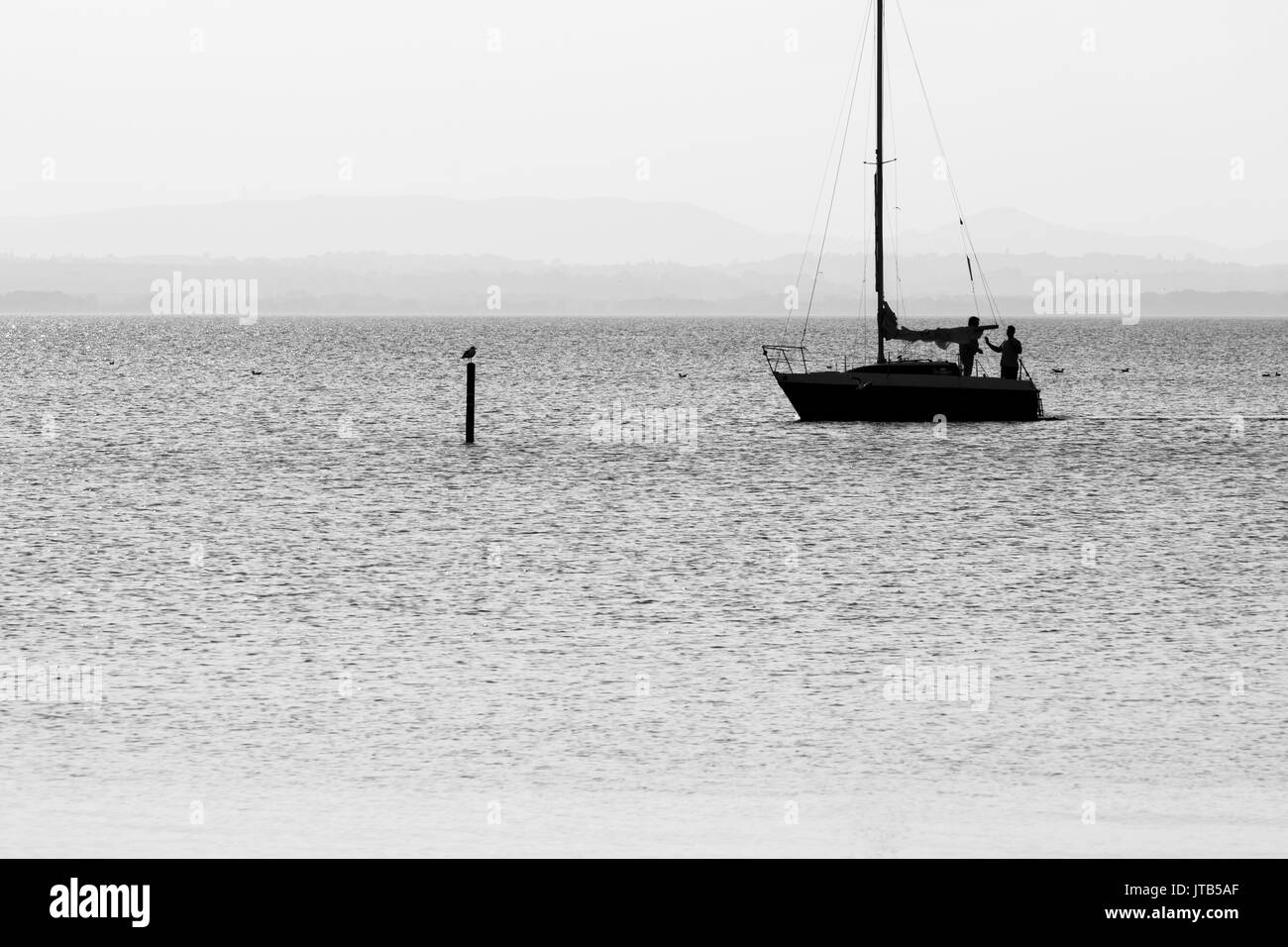 Silhouette von zwei Männer auf einem Boot über einen See, mit einem Vogel auf einer Stange vor Ihnen Stockfoto