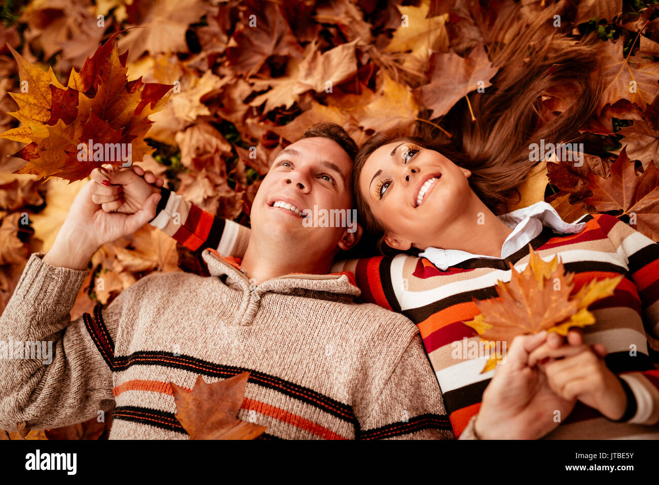 Schöne junge Paar im sonnigen Wald im Herbst Farben. Sie liegen auf dem Boden mit Blättern bedeckt und genießen. Stockfoto