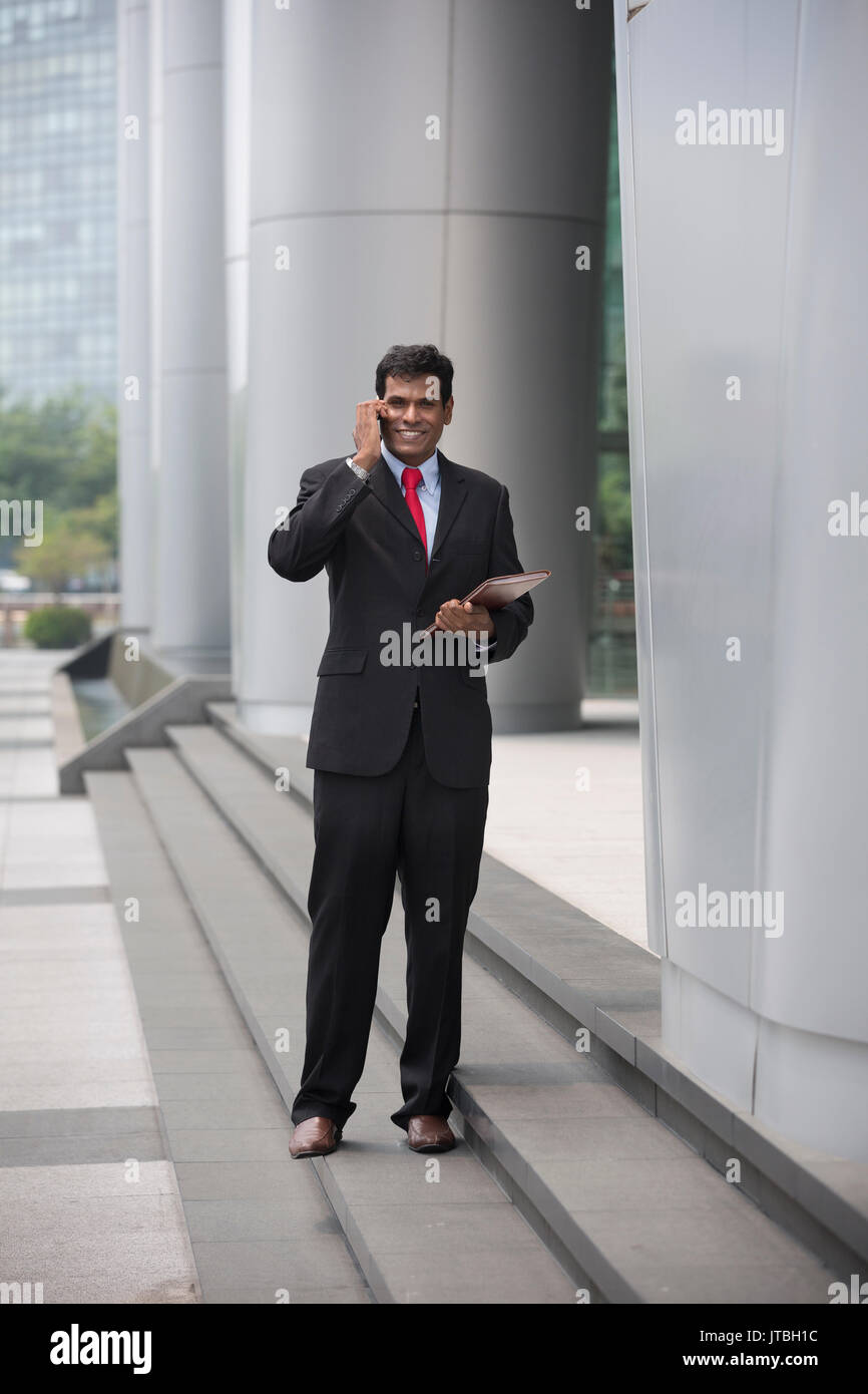 Indischer Geschäftsmann über sein Smartphone im Freien in einer asiatischen Stadt. Stockfoto