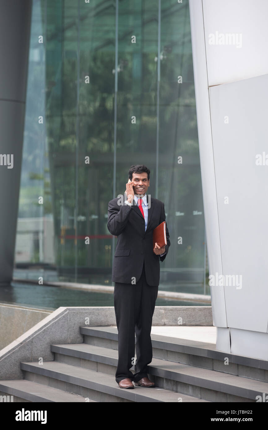 Indischer Geschäftsmann über sein Smartphone im Freien in einer asiatischen Stadt. Stockfoto