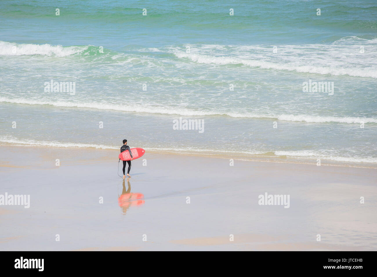 Ein einsamer Surfer mit einem roten Surfboard zu Fuß ins Meer. Newquay, Cornwall. Stockfoto