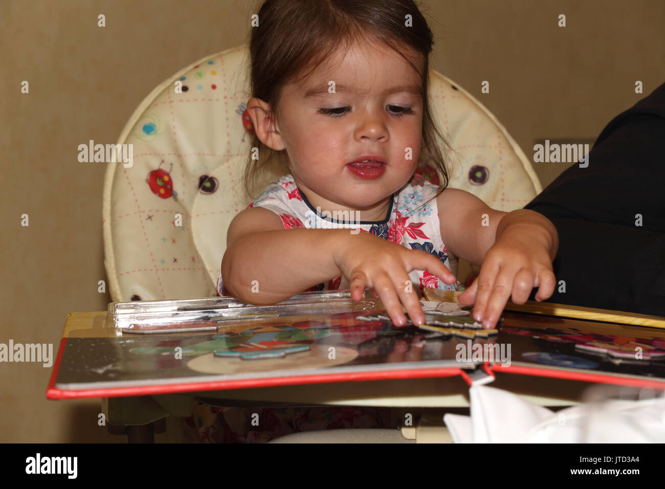 Kleinkind auf der Suche nach puzzle Buch in hoher Stuhl England Stockfoto