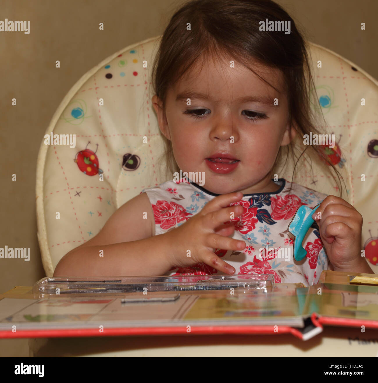 Kleinkind auf der Suche nach puzzle Buch in hoher Stuhl England Stockfoto