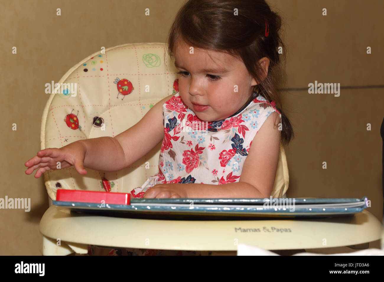 Kleinkind suchen im Buch in hoher Stuhl England Stockfoto