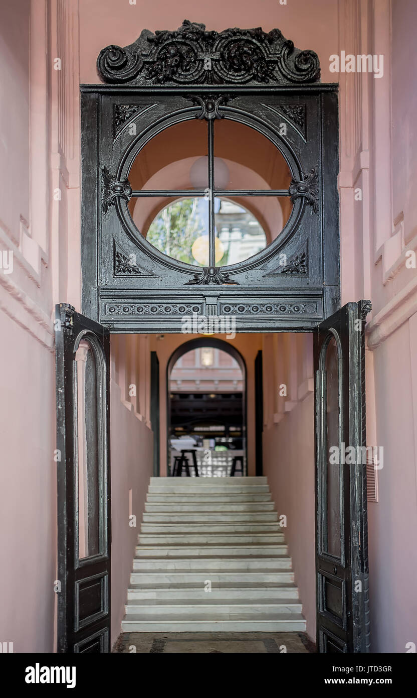 Eingang zum Restaurant mit dunklen, hölzernen Türen und einem runden Fenster mit Mustern. Es gibt rosa Wände, Treppen zu der Halle mit einem Bogen Tür. Ve Stockfoto