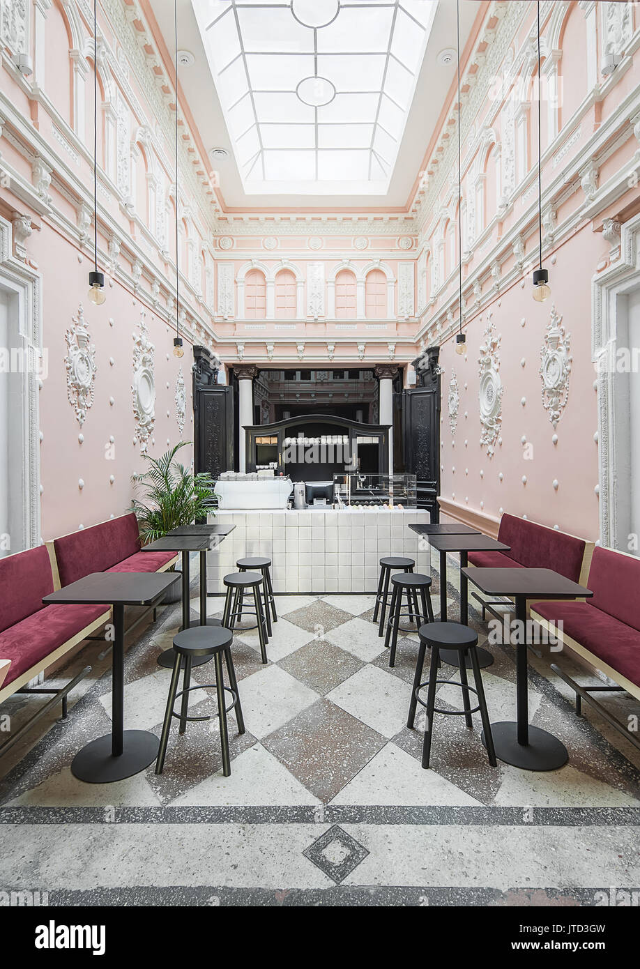 Kaffee Zone in der antiken Restaurant mit weißen Stuckverzierungen auf dem rosa Wände und große Fenster an der Decke. Es gibt rote Sofas, Fliesen- Rack wit Stockfoto