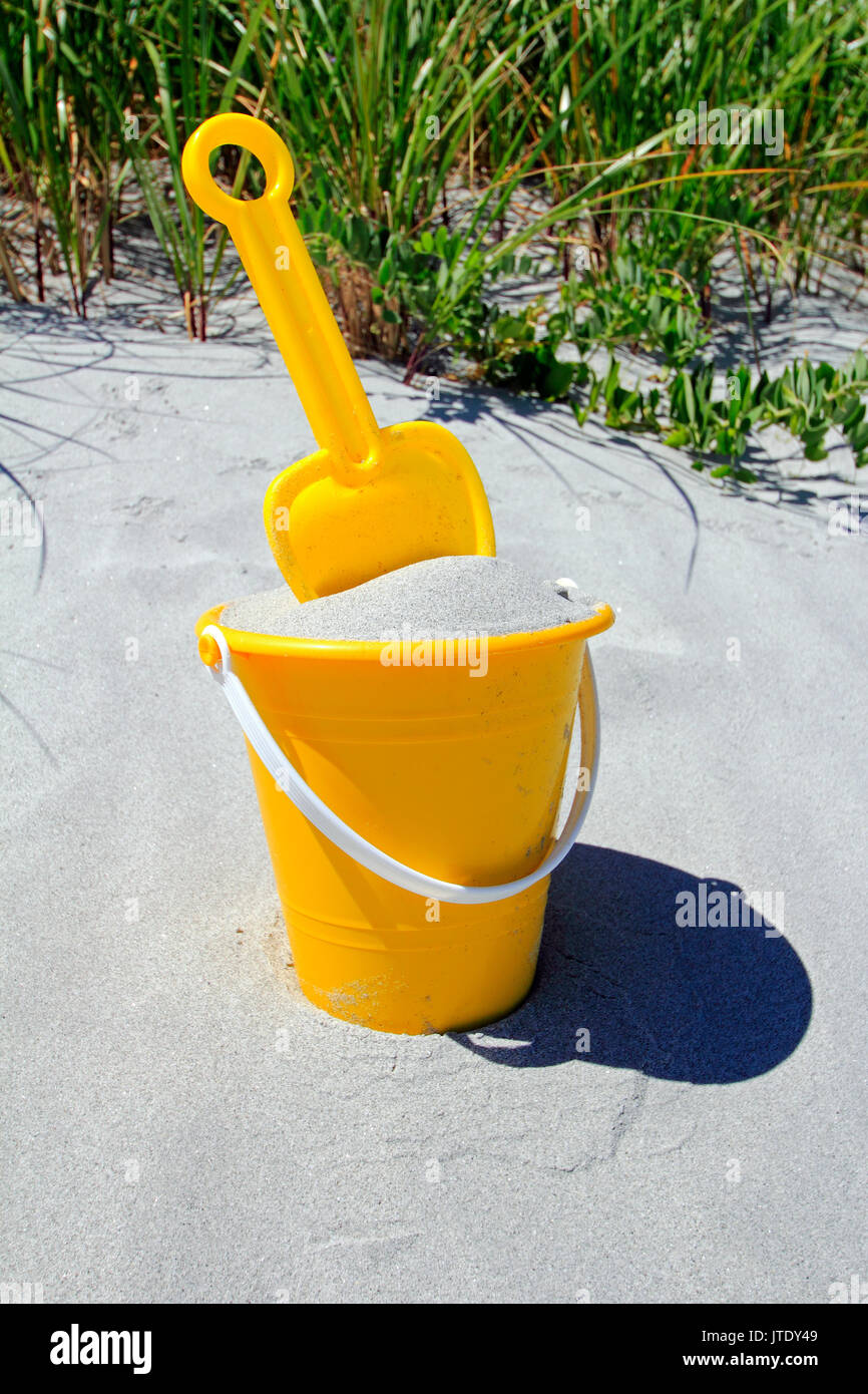 Ein Kind im gelben Eimer mit Sand und mit einer Schaufel an einem Strand gefüllt Stockfoto