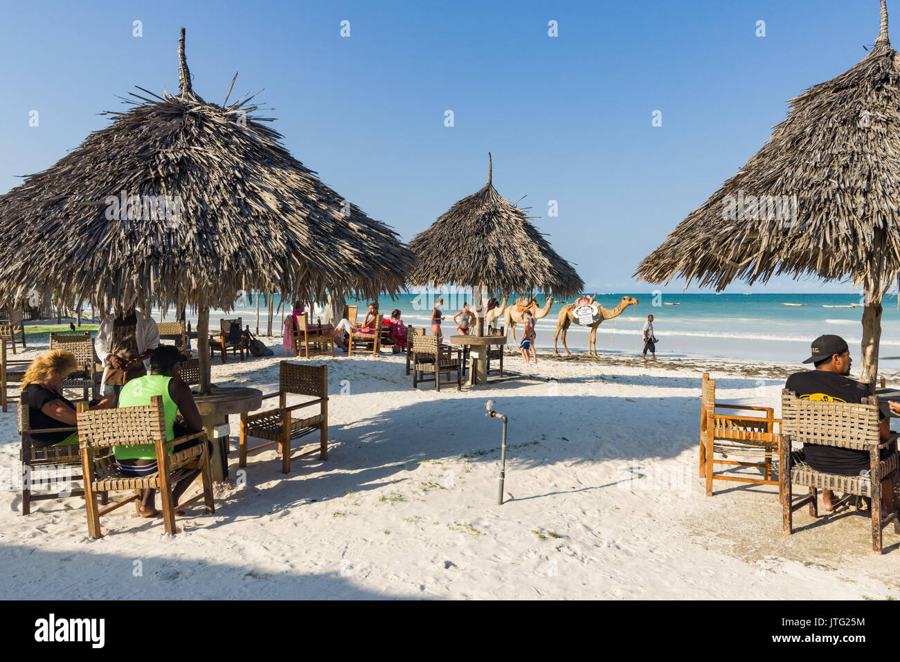 Touristen am Strand Ocean View Restaurant mit Palm thatch Tischen und Stühlen sitzen wie zwei Kamele Vergangenheit am Strand im Hintergrund laufen Stockfoto