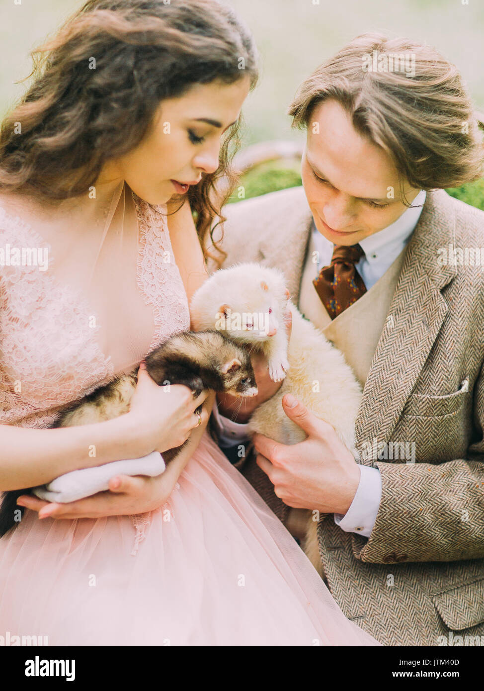 Das Foto der Vintage gekleidet Just married Holding die braunen und weißen Frettchen und genießen die Zeit im grünen Frühling Holz. Stockfoto