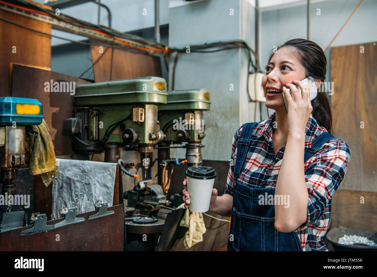 Attraktive Fräsmaschine weibliches Personal Holding/Paper Cup stand in bohren Abteilung ruht und mit mobilen Smart Phone zum Aufruf chatten Stockfoto