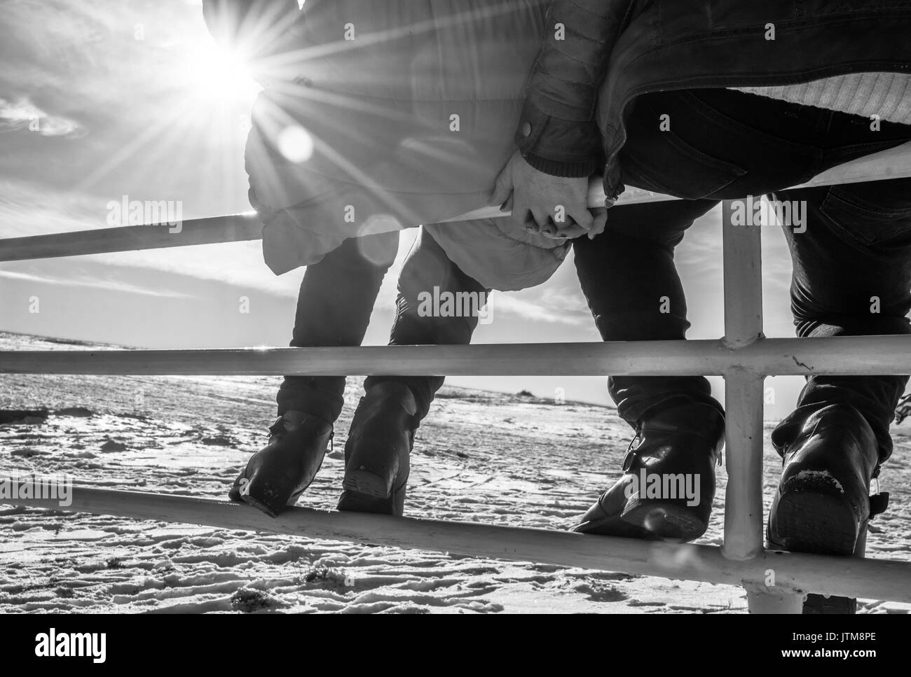 Paar in Liebe Hände halten Sitzen auf einem Metallzaun und genießen Sie die Wintersonne Stockfoto