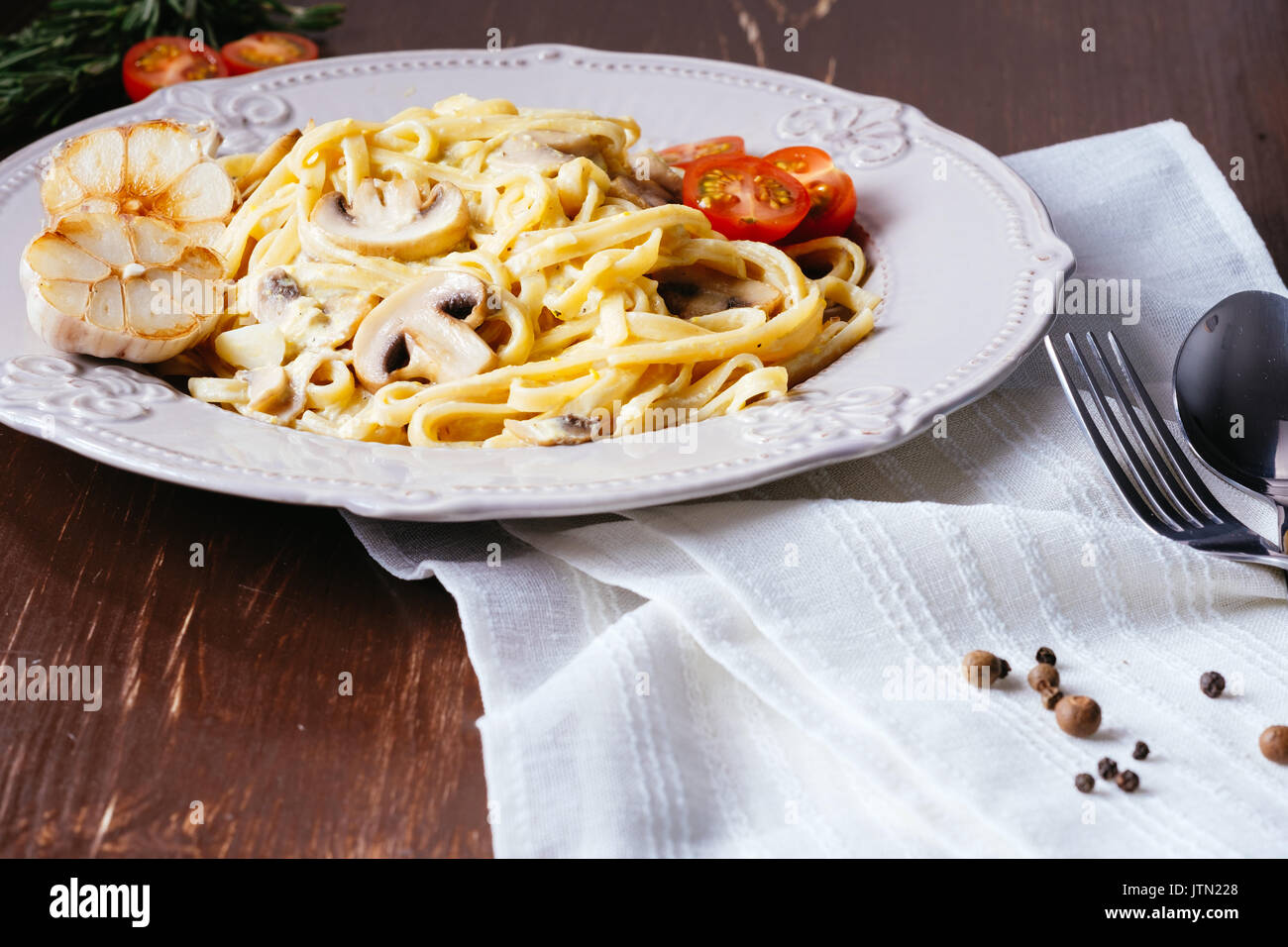 Cremige italienische Pasta mit Pilzen, Tomaten und Knoblauch. In einem Jahrgang Teller mit Besteck auf einem braunen Tisch mit einer Serviette und Gewürze Stockfoto