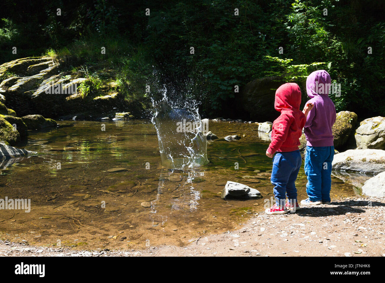 Zwei kleine Kinder werfen Steine ins Wasser Stockfoto