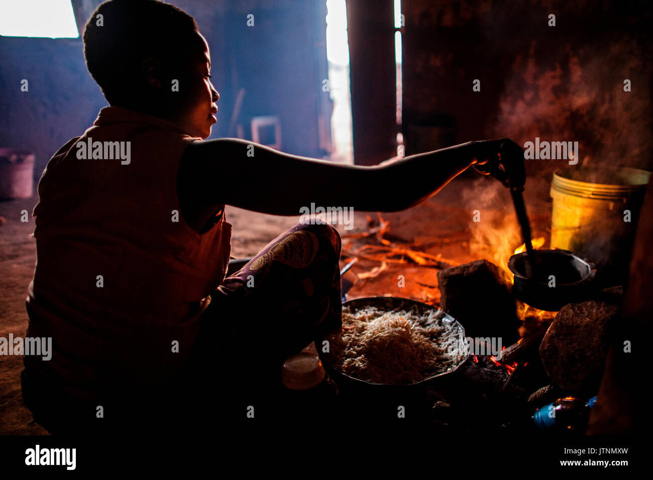 Ester Hodari, Alter 22 Jahre alt, kocht das Abendessen mit dem traditionellen 3-rock Koch Herd mit einem Feuer in der Mitte. Diese cookstoves verwenden eine Menge Kraftstoff, Brennholz, und viel Rauch erzeugen. Ester sagte uns, dass das Kochen mit dieser Art von Herd ihre Augen sind rot und Sie mussten oft eine Brust Husten. Ihre Kinder im Alter von 5, 2 und 3 Monaten werden oft mit ihr, als sie kocht. Ihre Schwägerin, shadya Dienstag, Alter 11, hilft ihr Kochen. Vor nicht allzu langer Zeit Esterâs 3 Monate alten einen Husten entwickelt, es wurde immer schlimmer und so nahmen sie Stockfoto