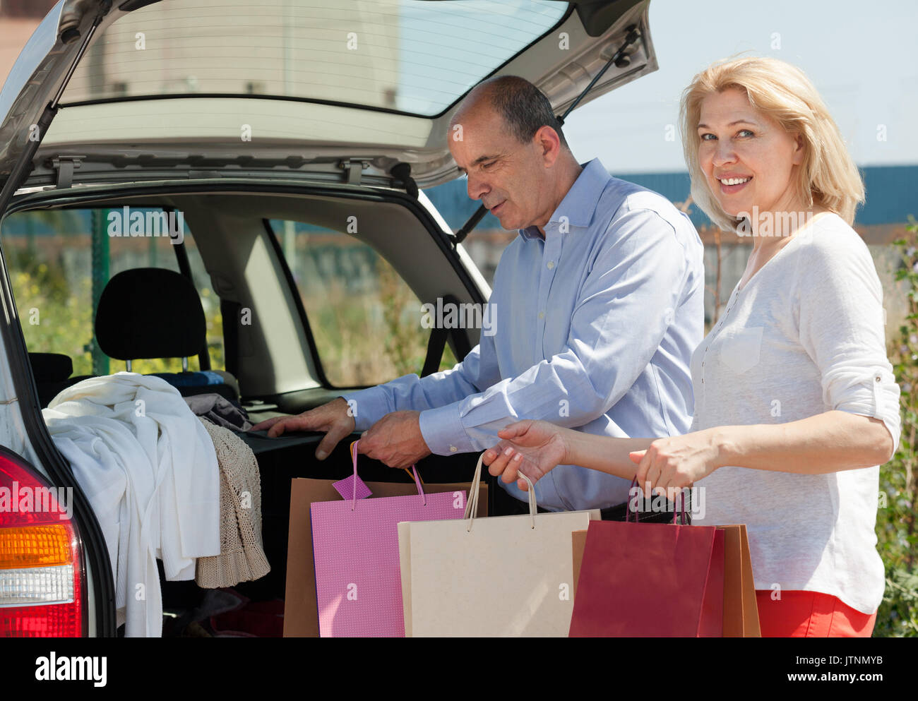 Gerne reifer Mann und Frau mit Taschen in den Händen in der Nähe ein Auto Stockfoto