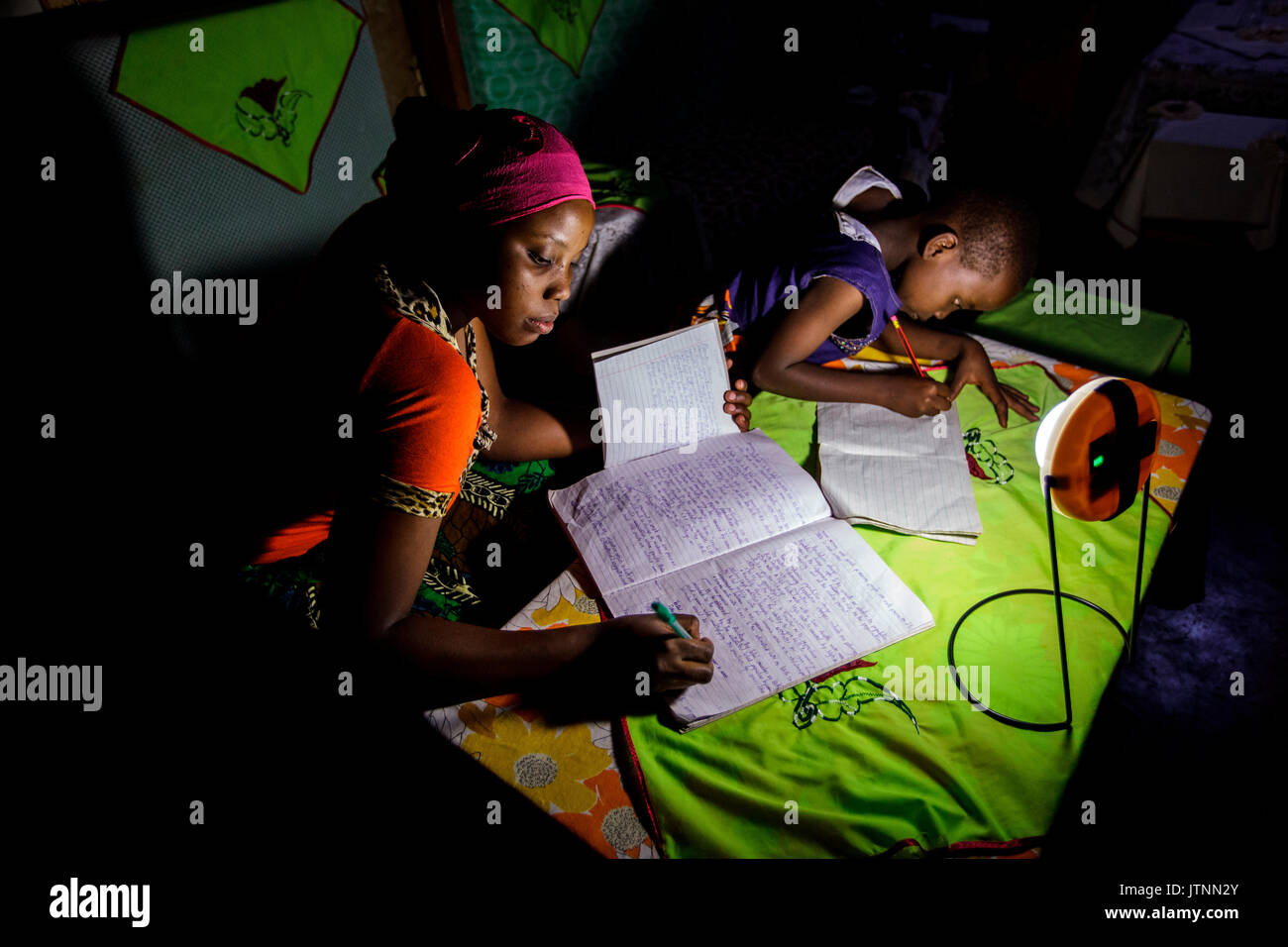Mforo, Tansania, einem Dorf in der Nähe von Moshi, Tansania. Der Einsatz einer Solar Schwester solar Lantern mehrere von Solar Schwester Unternehmer Fatma Mzirayâs Kinder nachts studieren. Ihre ältere Tochter Zainabu Ramadhani Alter 19 ist auf der linken und mittleren Tochter Sabrina Ramadhani, Alter 8 ist auf der rechten Seite. Fatma Mziray ist ein Solar Schwester Unternehmer Wer verkauft beide Sauber cookstoves und Stockfoto