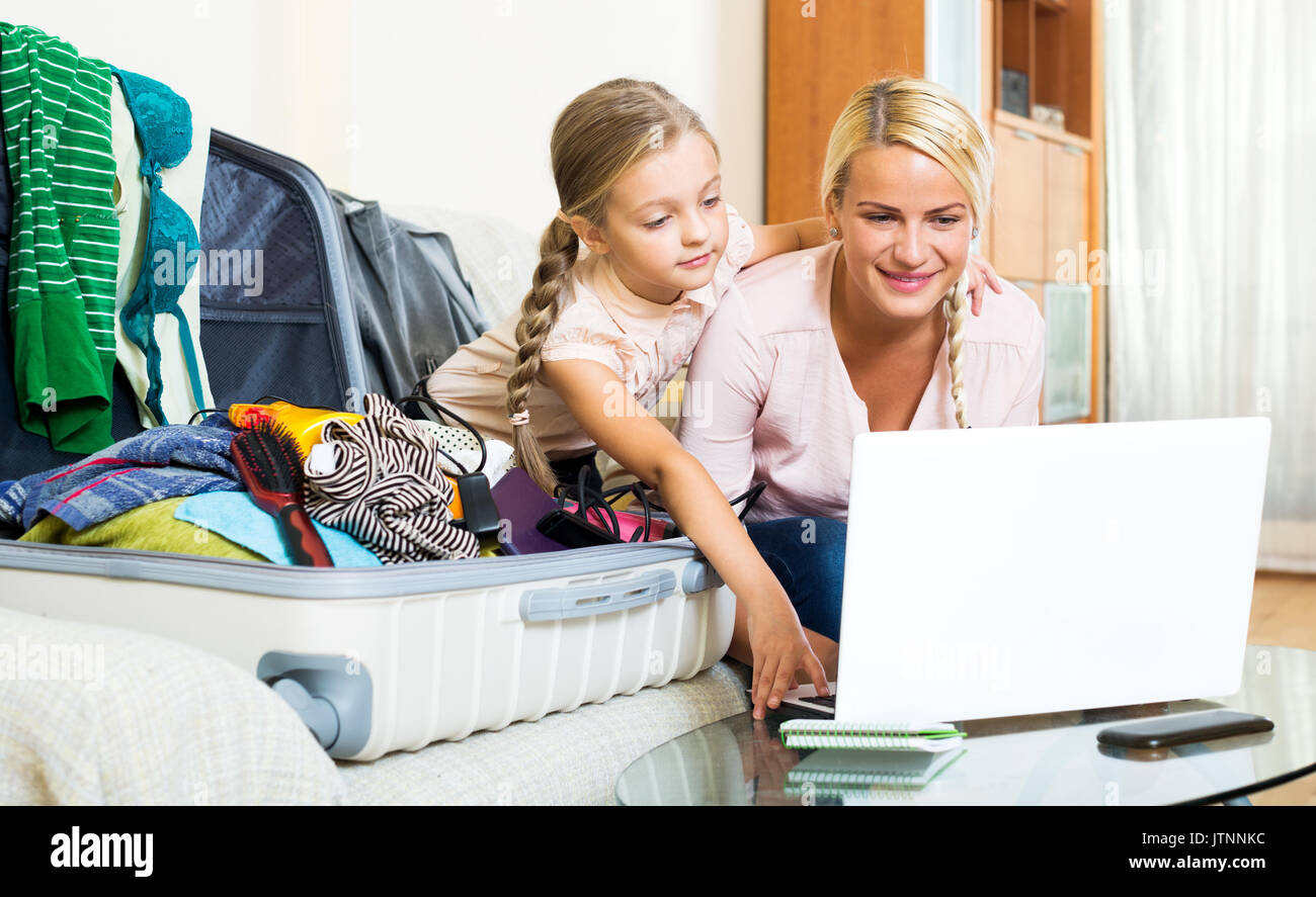 Glückliche junge blonde Mutter und Tochter mit Gepäck im Web surfen Stockfoto