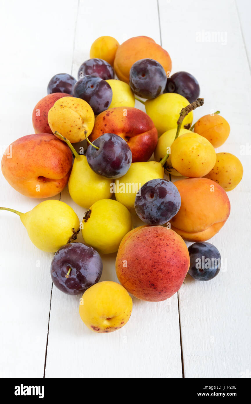 Ein Haufen von saftigen Sommer Früchte auf weißem Holz- Hintergrund (Pflaumen, Aprikosen, Birnen). Ernte aus dem Garten. Eine natürliche Quelle von Vitaminen. Stockfoto