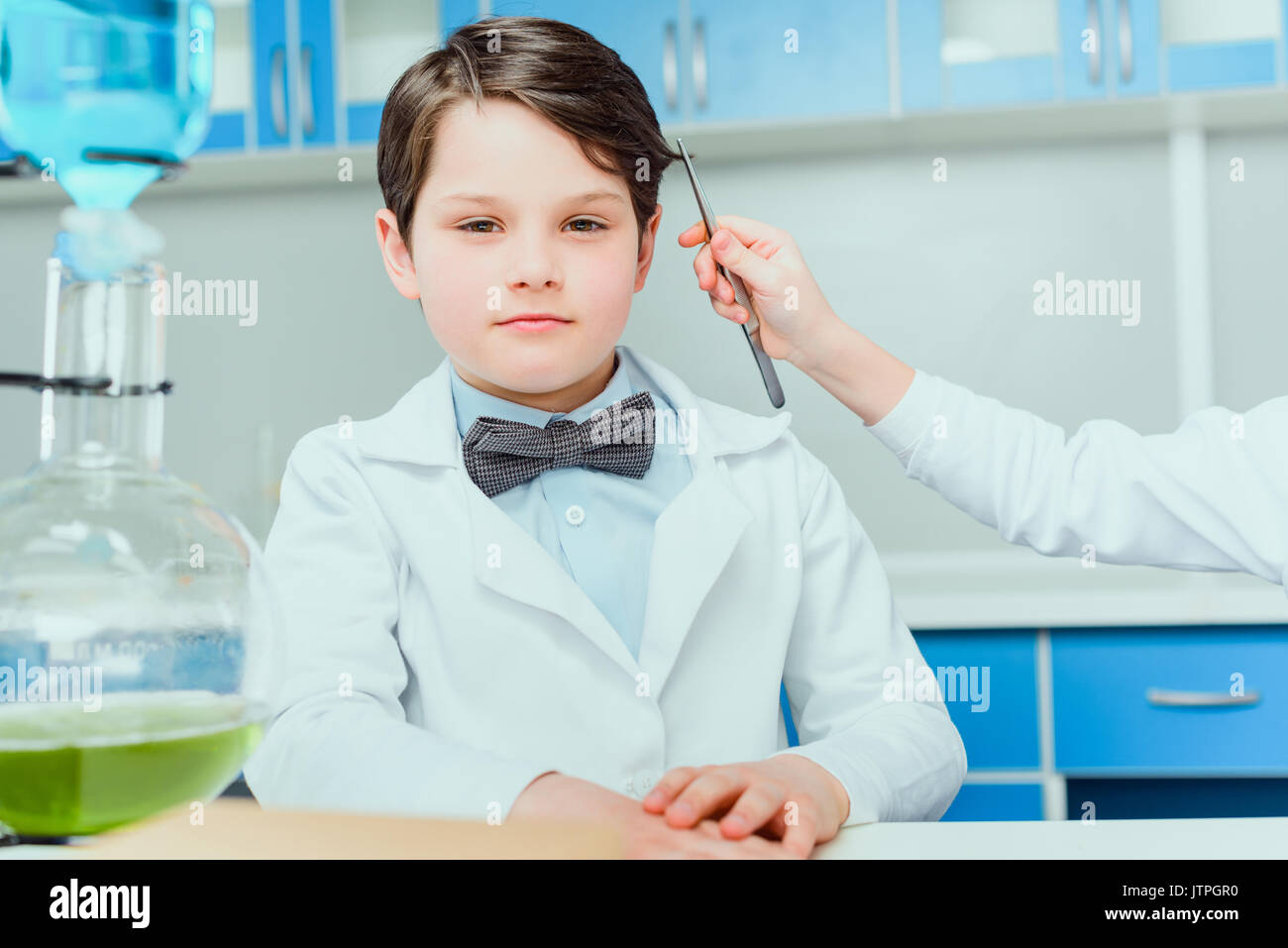 7/8 Schuß von kleinen Wissenschaftler mit einer Pinzette die Haare Probe von Jungen im weißen Mantel in der Wissenschaft Labor sitzen Stockfoto