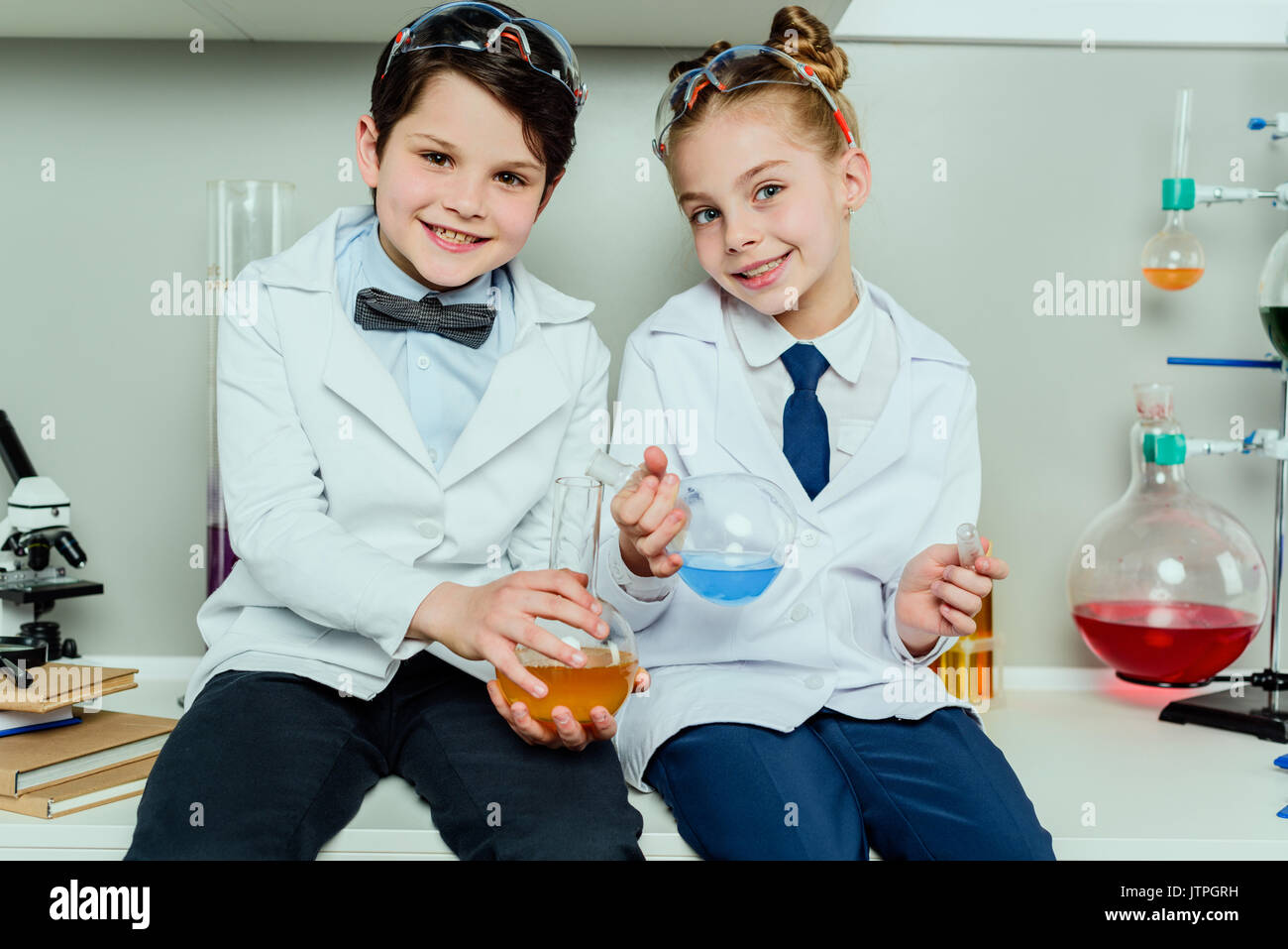 Schüler in weißen Kitteln holding Reagenzien in Flaschen in der Wissenschaft Labor sitzen Stockfoto