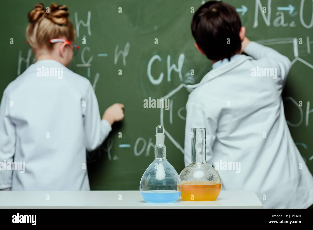 Rückansicht der Jungen und Mädchen in laborkitteln Zeichnen chemischer Formeln auf der Schiefertafel, Wissenschaft Schule Konzept Stockfoto
