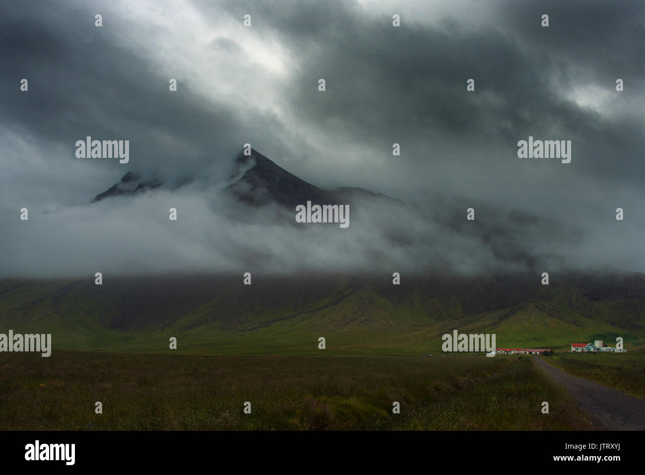 Kleine farm gegen eine Wolke fallenden Berg inmitten der dramatischen, vulkanische, subalpine Landschaft von Island Stockfoto