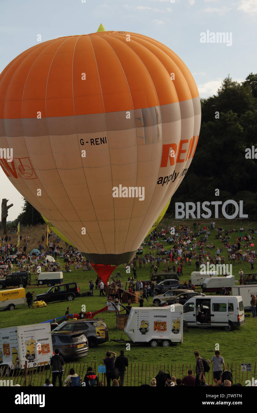 Aufgeblasener Heißluftballon immer noch auf dem Boden, sondern vorbereiten, mit großen dekorativen "Bristol" Schild hinter sich und Sammeln von Menschenmassen, an der Bristol International Balloon Fiesta, Long Ashton, Bristol. 10. August 2017. Stockfoto